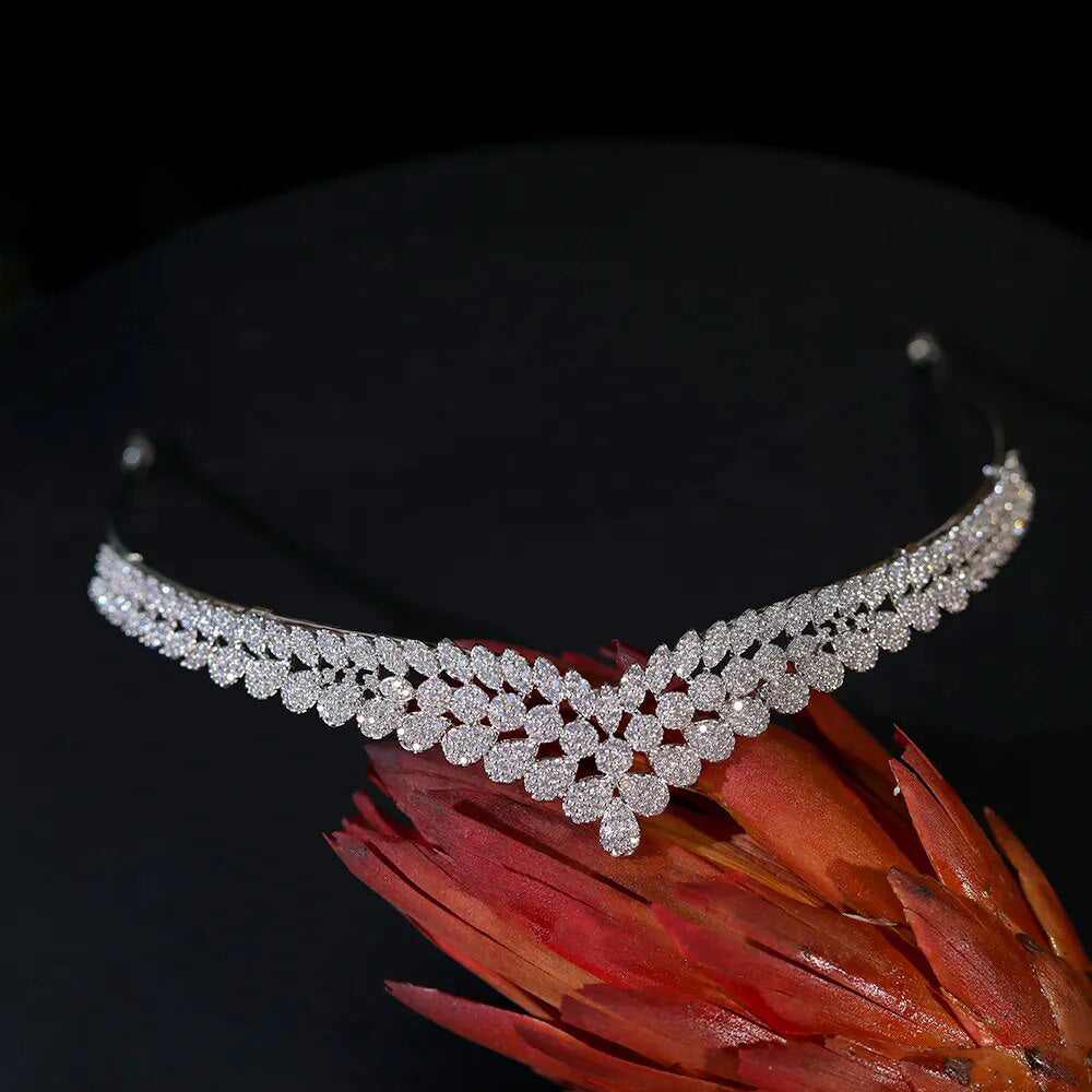 Direct overhead flat lay view of a V-shaped luxury cubic zirconia wedding headpiece resting gracefully on a reddish tropical flower stem.