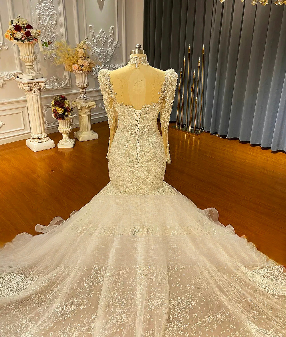 Detailed back view of the bodice on a luxury mermaid wedding gown, showing the sheer illusion back panel, corset lacing, and long sleeves with crystal detailing.