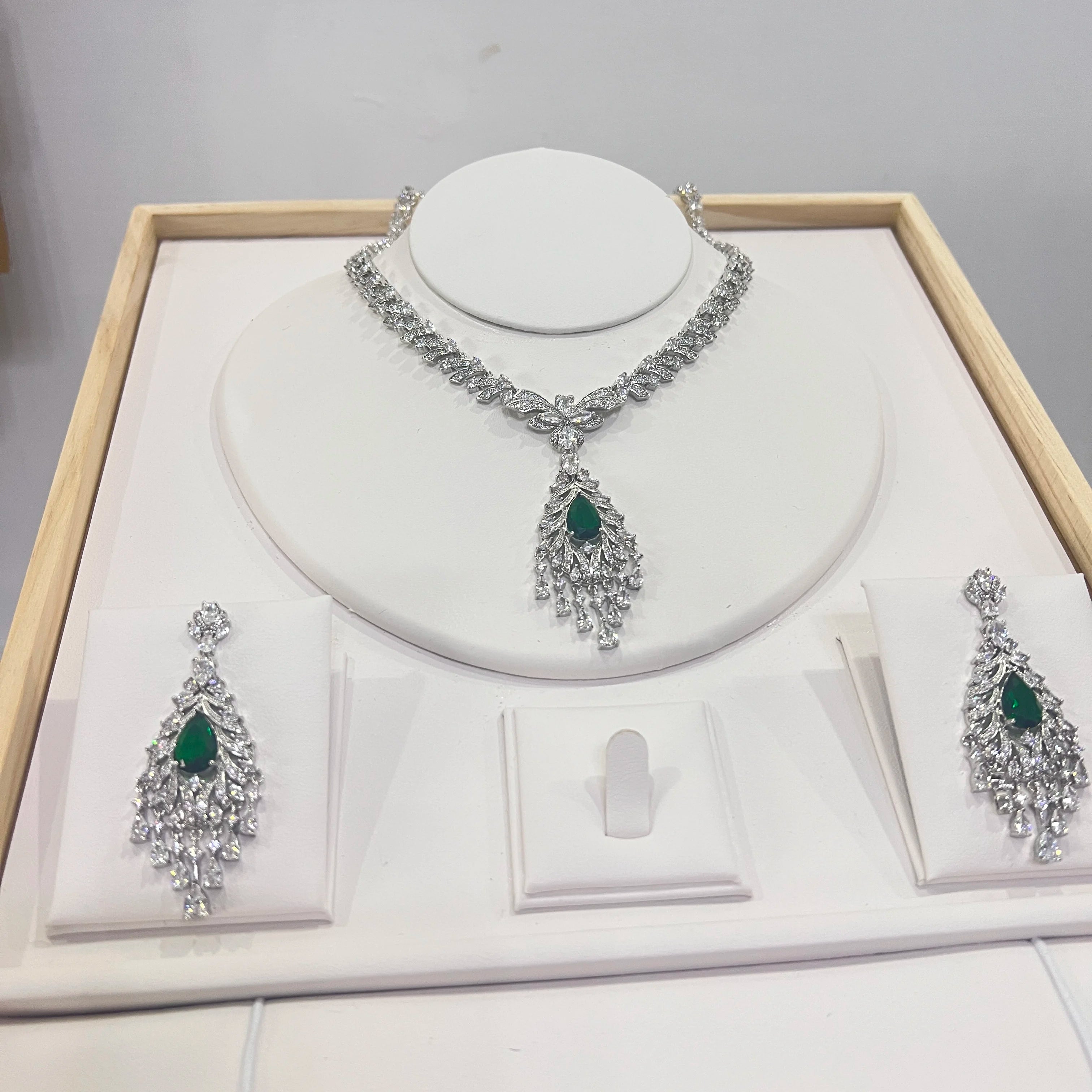 High-end emerald green crystal tassel necklace and matching drop earrings presented on a boutique display tray