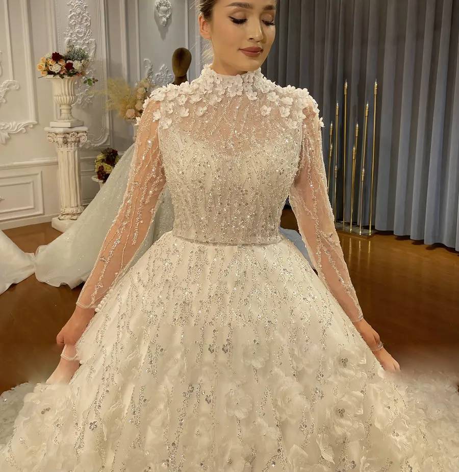 Close-up detail of a beaded wedding dress bodice showing 3D floral neck embellishments and shimmering sequin embroidery.