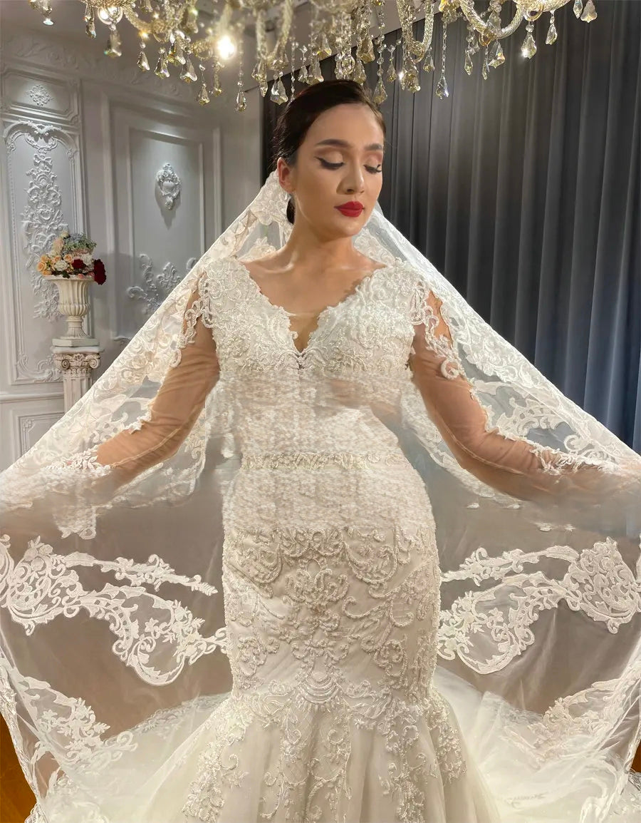 Close-up shot of a stunning lace mermaid bridal gown showcasing the intricate floral embroidery, V-neckline, and a matching long lace bridal veil.