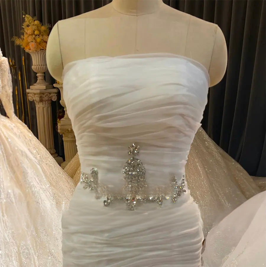 Close-up detail of the off-white wedding dress bodice on a mannequin, focusing on the delicate ruched organza layers and the luxury crystal-beaded waist design.