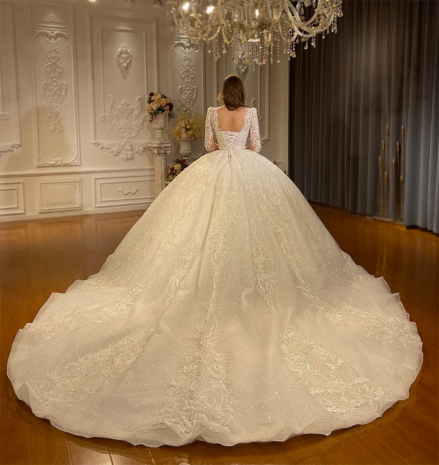 Back view of an elegant off-white wedding gown on a model, highlighting the traditional lace-up corset back and an expansive, shimmering train.