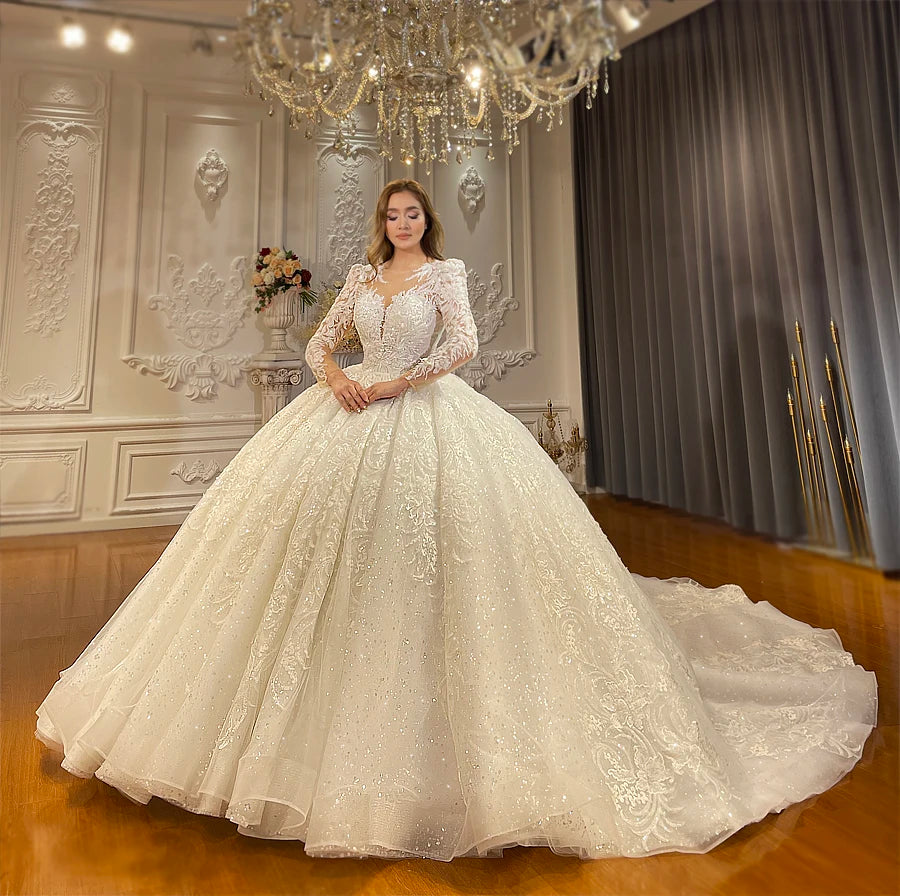 Full-length front view of a stylish off-white wedding gown with a structured beaded bodice, illusion neckline, and a wide sparkling organza skirt.
