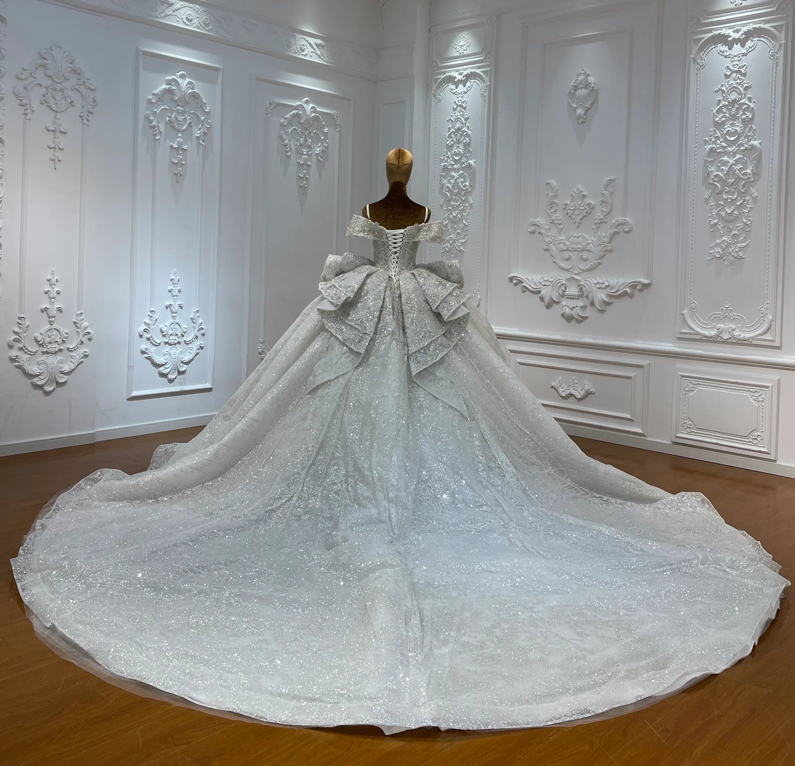 Back view of a sequined bridal gown highlighting a structured lace-up corset back and a dramatic, shimmering cathedral-length train.