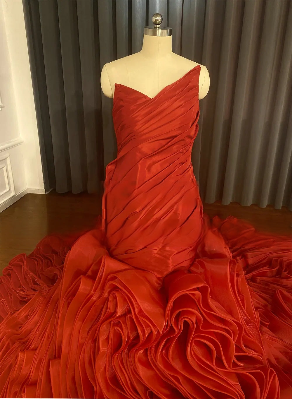 Close-up of the elegant red satin wedding dress bodice on a mannequin, detailing the ruched, one-shoulder design and the start of the ruffled skirt.