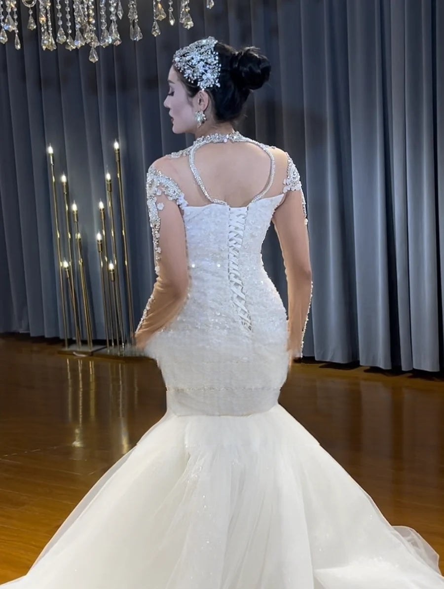 Rear view of a beaded mermaid bridal gown highlighting an elegant illusion back with a traditional lace-up corset closure and the cascading start of a white tulle train.