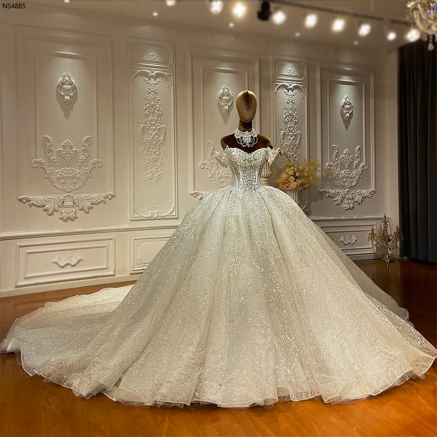 Mannequin displaying a luxury beaded mermaid wedding gown with detachable off-the-shoulder straps, a structured sweetheart bodice, and a massive, glittering circular train.