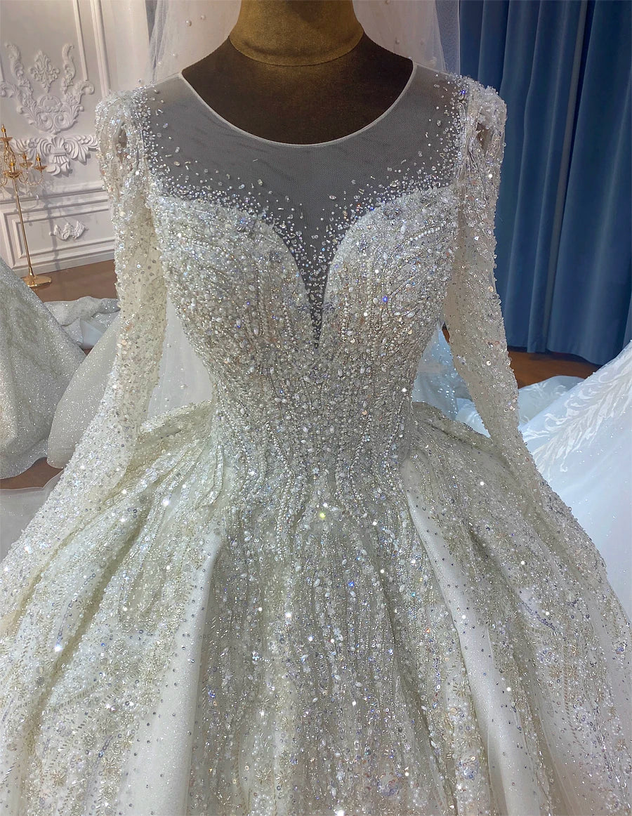 Close-up of the real hand work on a luxury wedding dress, showing the intricate premium crystal patterns, pearl accents, and shimmering beadwork on the illusion neckline and sleeves.