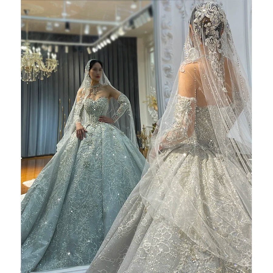 A bride showcases a luxury lace crystal wedding dress in a shimmering silver hue, featuring an intricately embellished sweetheart bodice and removable long sheer sleeves, captured through a mirrored reflection in an elegant bridal boutique.