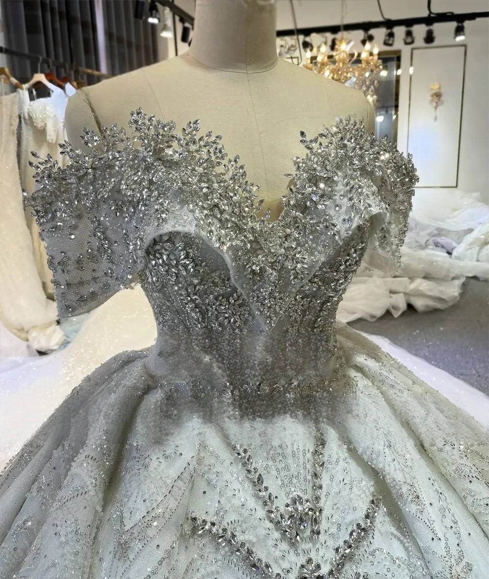 High-detail close-up of the bodice on the luxury off-the-shoulder wedding gown, featuring premium crystal and pearl beading along the plunging neckline and sleeves.