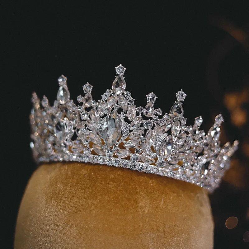 Front view of a glamorous crystal headband wedding crown displayed on a textured gold velvet stand.