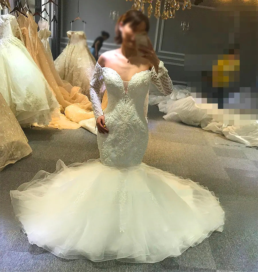 Front view of a white off-the-shoulder mermaid bridal gown with intricate beaded lace and a voluminous layered organza skirt.