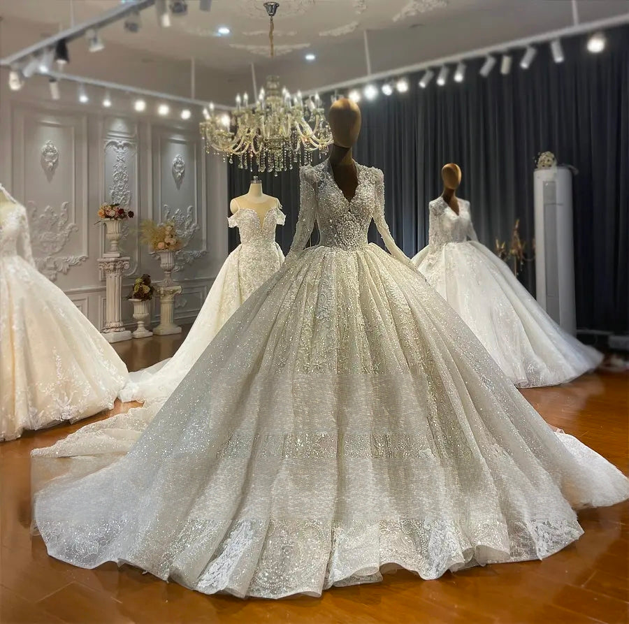 Full front angle view of a luxury long-sleeve lace ball gown wedding dress with a deep V-neckline, emphasizing the grand, shimmering flared skirt silhouette.
