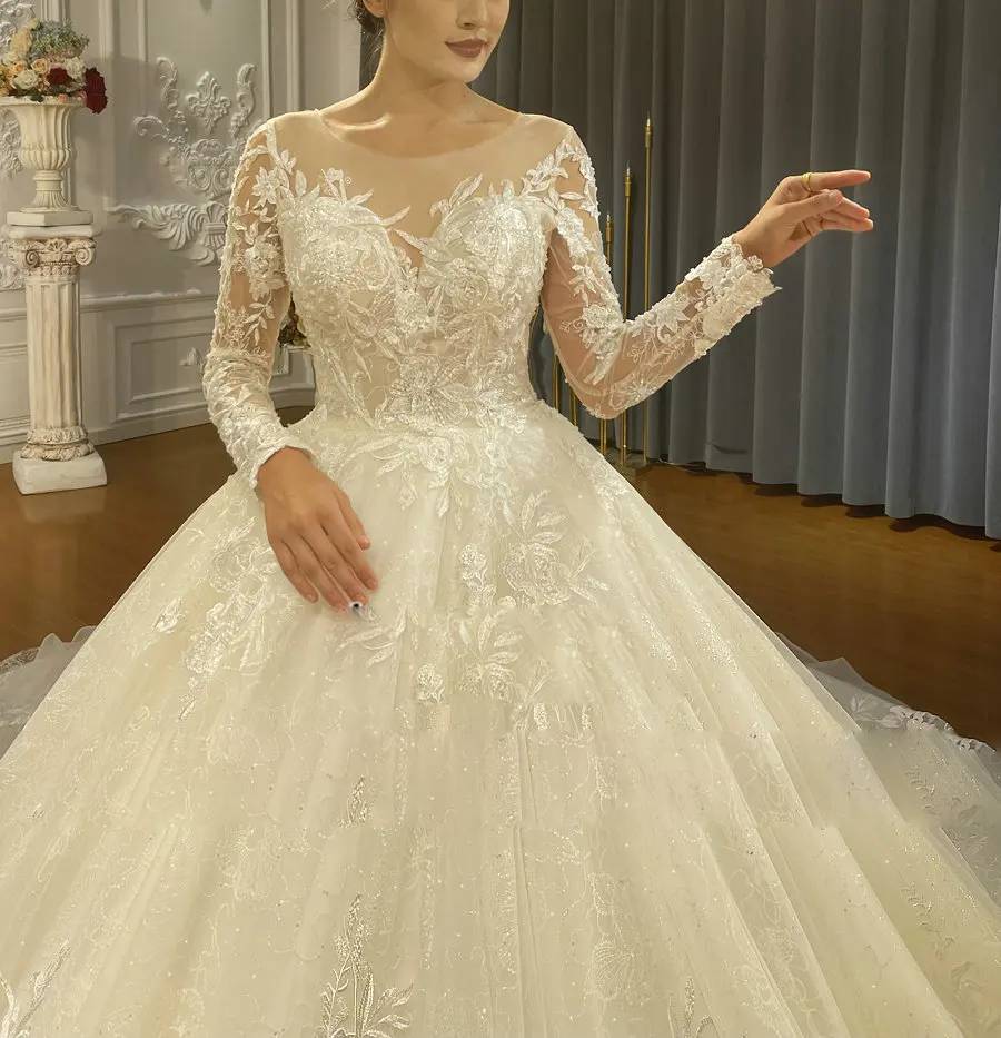 Close-up detail of a bridal gown's illusion neckline and long sleeves adorned with intricate white floral lace appliqués.