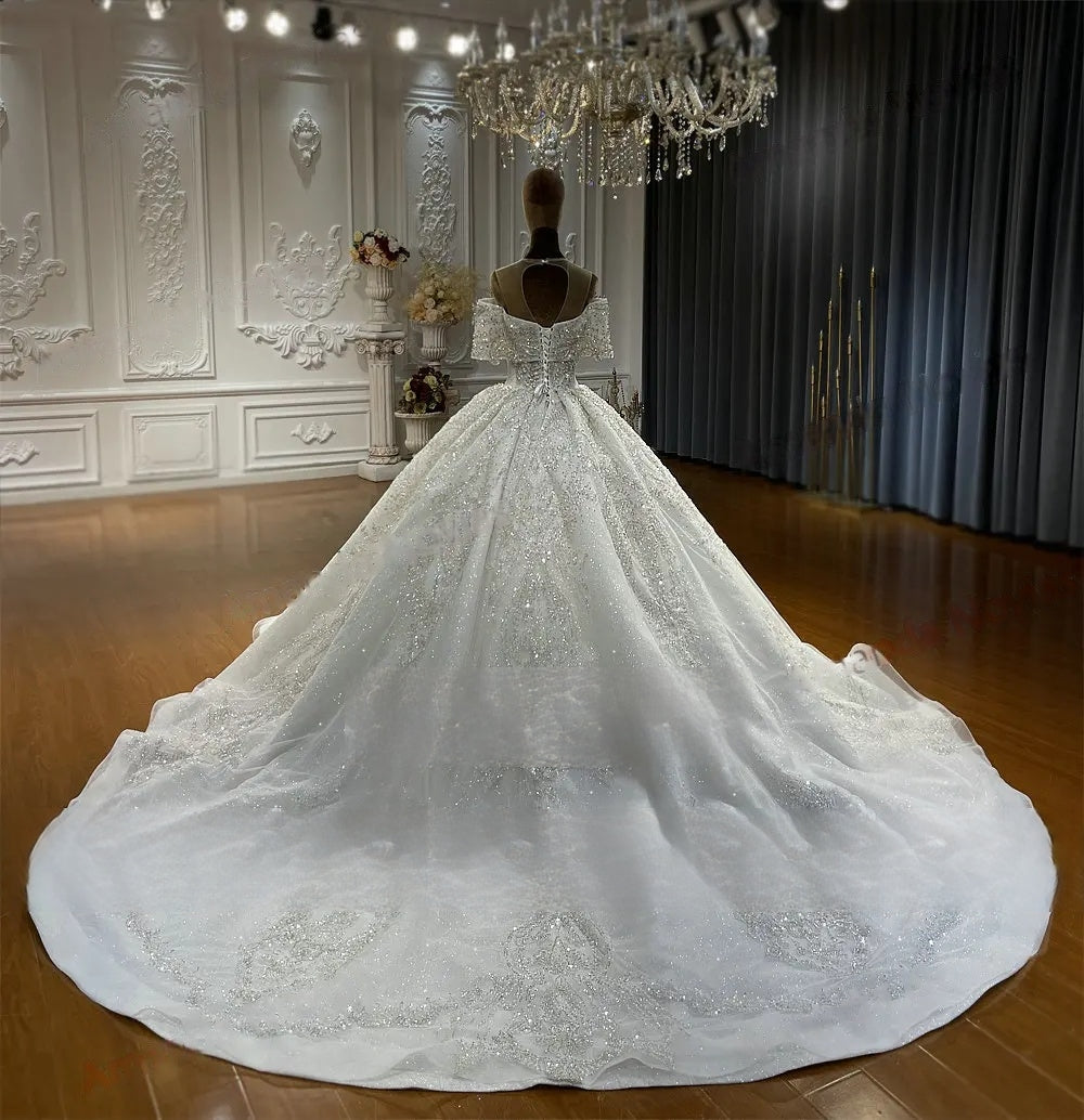 Rear perspective of the elegant off-the-shoulder wedding gown on a mannequin, showcasing the illusion keyhole back, corset lacing, and long, heavily beaded train.