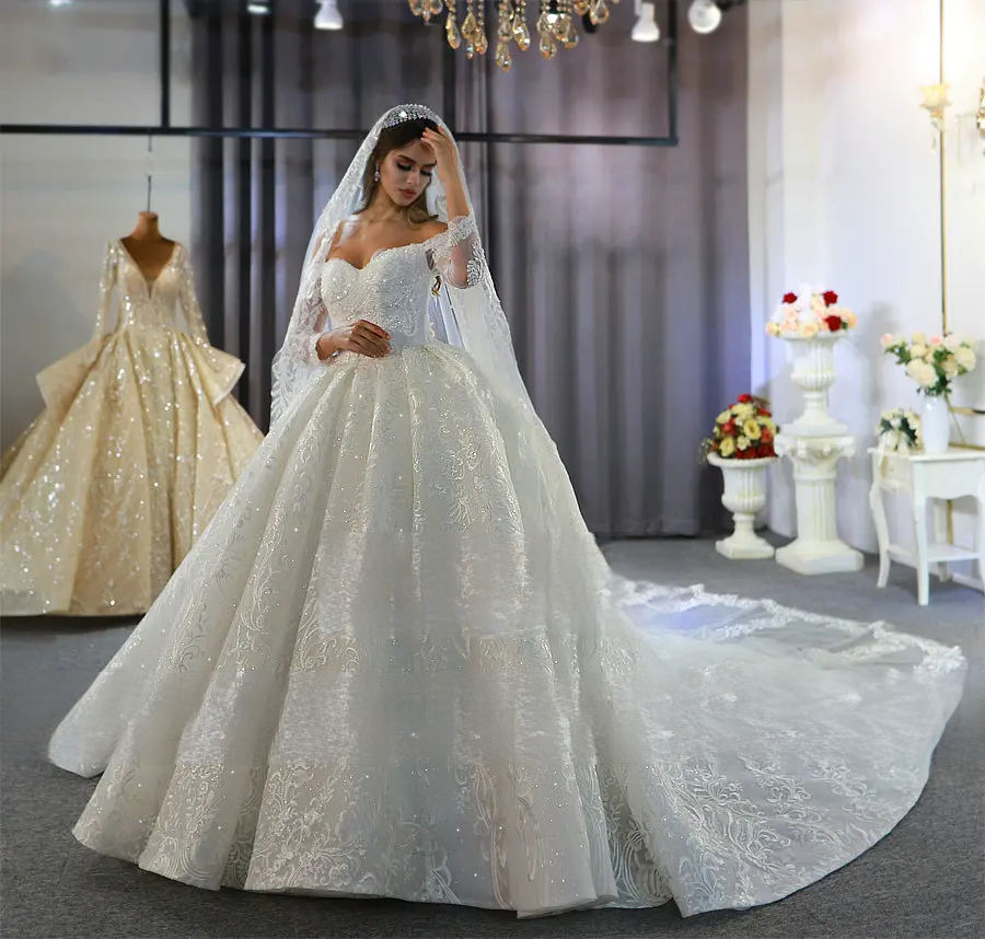 Full-length front view of an elegant off-the-shoulder wedding dress with long sheer lace sleeves and a voluminous ball gown skirt.