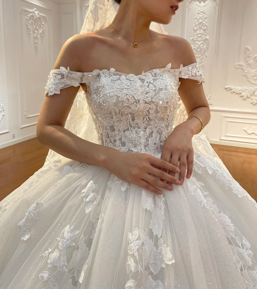 Close-up detail of an off-the-shoulder wedding dress bodice showcasing delicate floral lace appliqués and a sweetheart neckline.