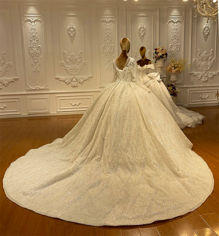 Back angle view of a luxury pearl-detailed wedding gown on a mannequin, displaying the voluminous, sparkling circular train and intricate sleeve embroidery.