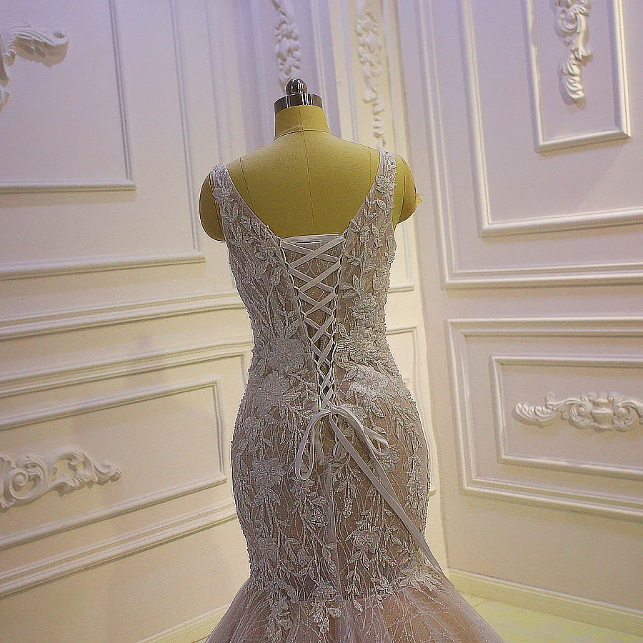Close-up of the back of a lace mermaid bridal gown on a mannequin, showing a traditional corset-style lace-up closure and delicate floral embroidery.