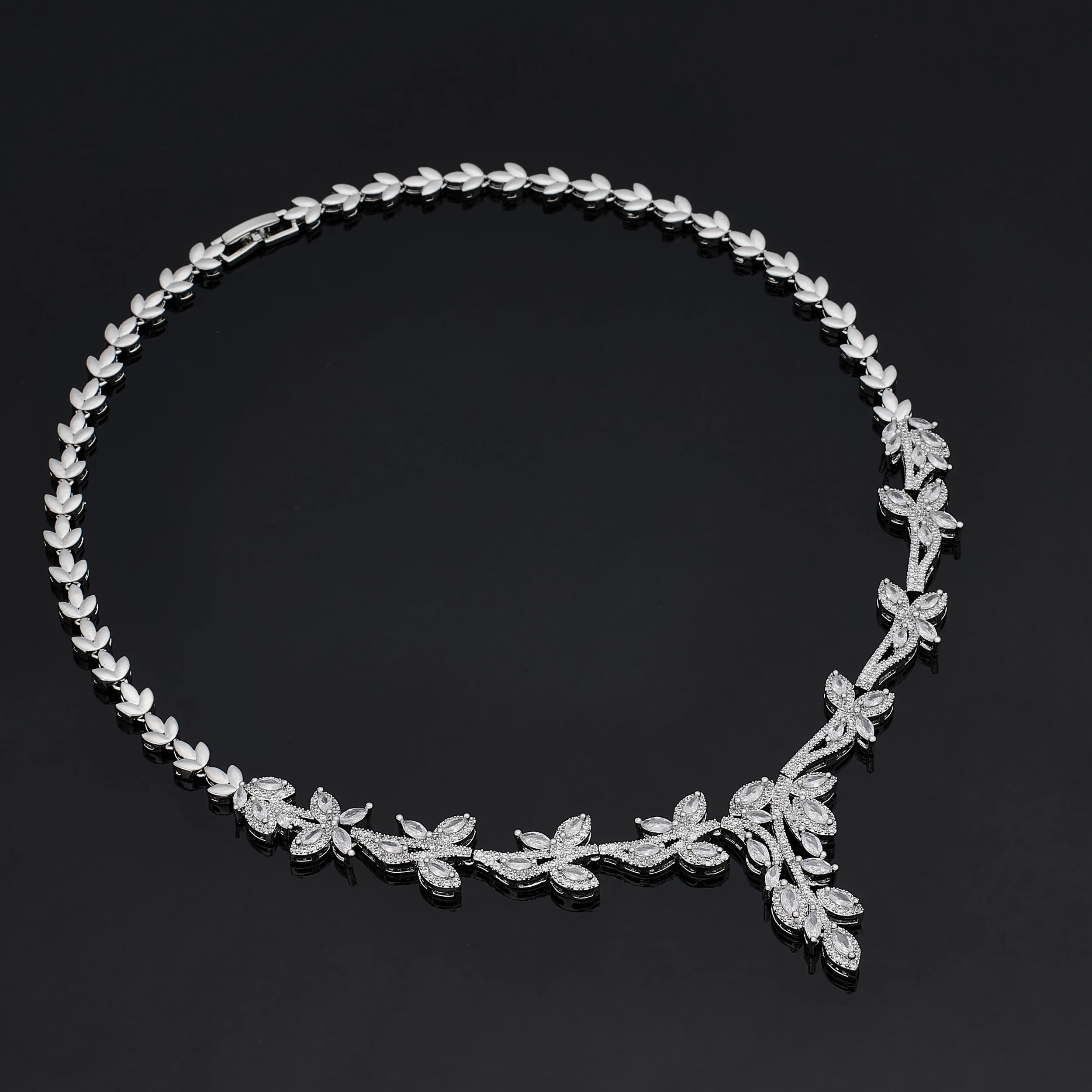 Overhead view of a silver branch-motif cubic zirconia wedding necklace, highlighting its detailed leafy pave structure on a dark reflective surface.