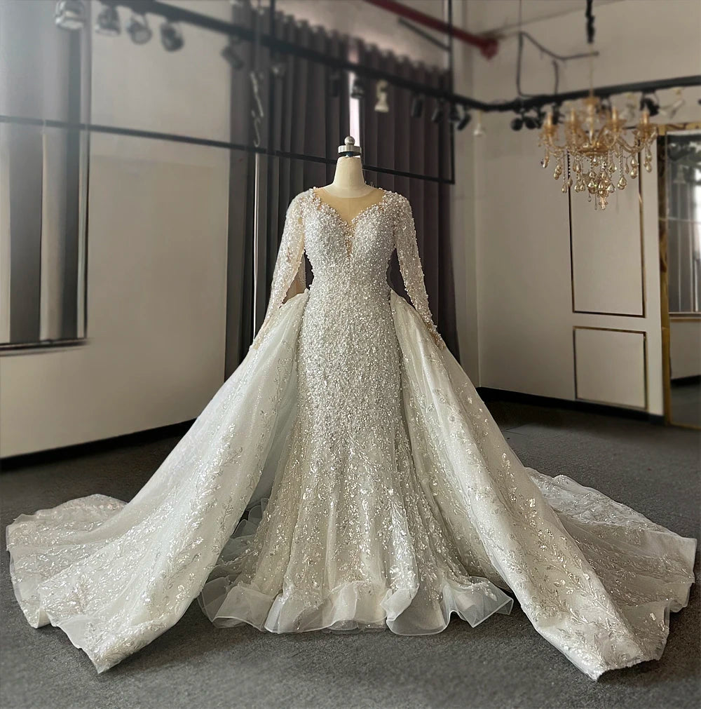 A grand back view of the two-in-one wedding dress, emphasizing the expansive, glittery detachable overskirt and the long, sweeping silhouette in a bridal showroom.