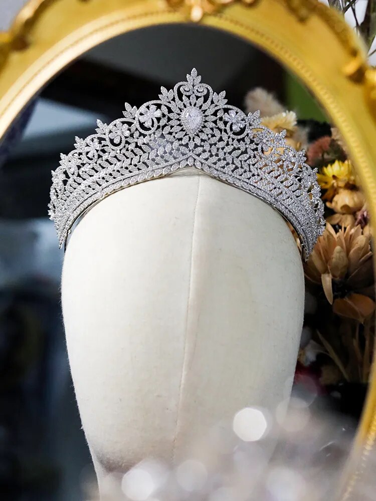 A premium silver zirconia bridal tiara crown displayed on a white mannequin head piece in front of a golden vintage mirror.