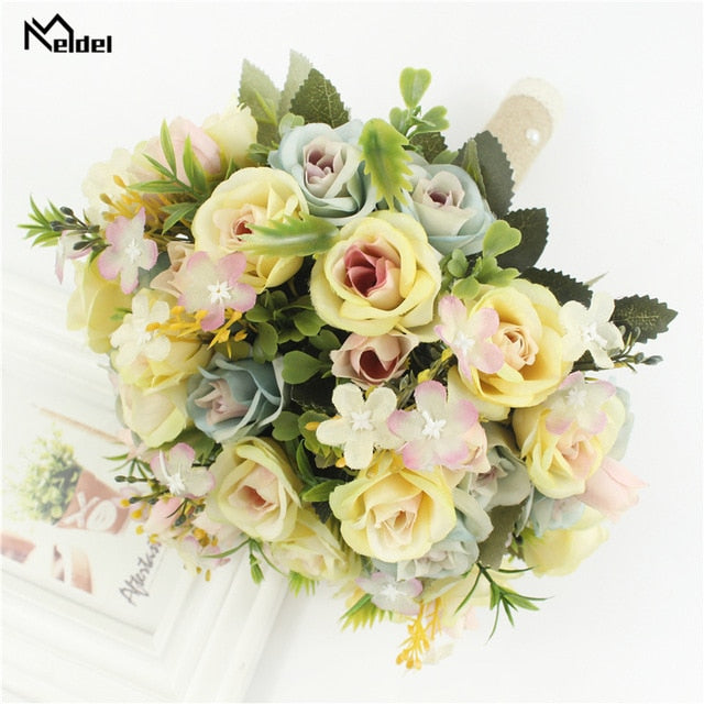 Overhead flat lay view of a colorful handmade bridal wedding bouquet featuring pastel yellow, dusty blue, and soft pink silk roses accented with mini purple blossoms.