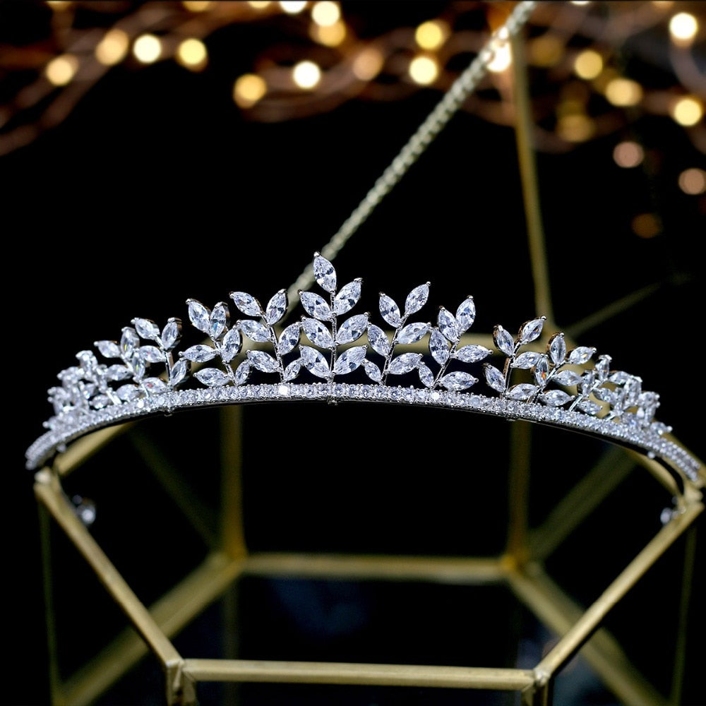 Front view of the intricate marquise cubic zirconia bridal tiara crown, displaying symmetrical branching metal leaf accents resting on a modern geometric gold stand.
