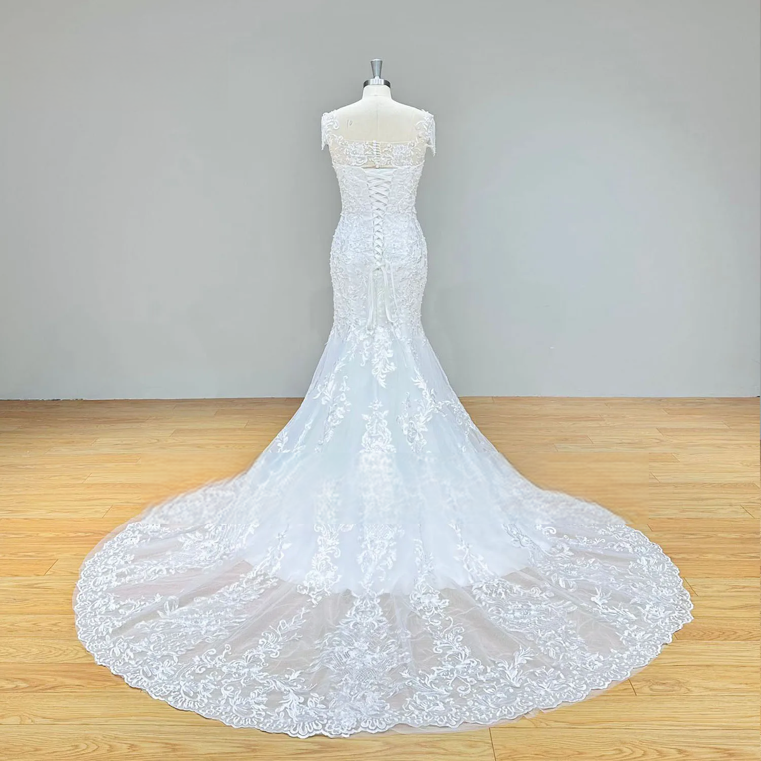Rear view of a fitted mermaid wedding dress on a mannequin featuring an elegant lace-up corset back and a beautiful lace-trimmed train.