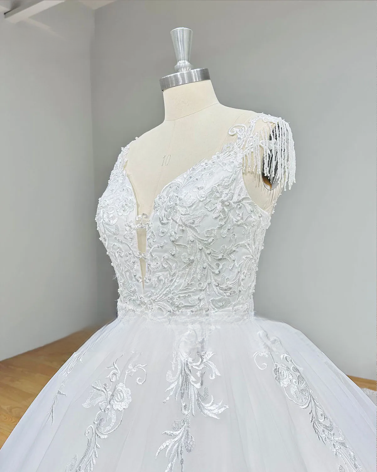 Detailed side view of a bridal bodice on a mannequin with sparkling beading, sequins, and delicate beaded fringe shoulder accents.