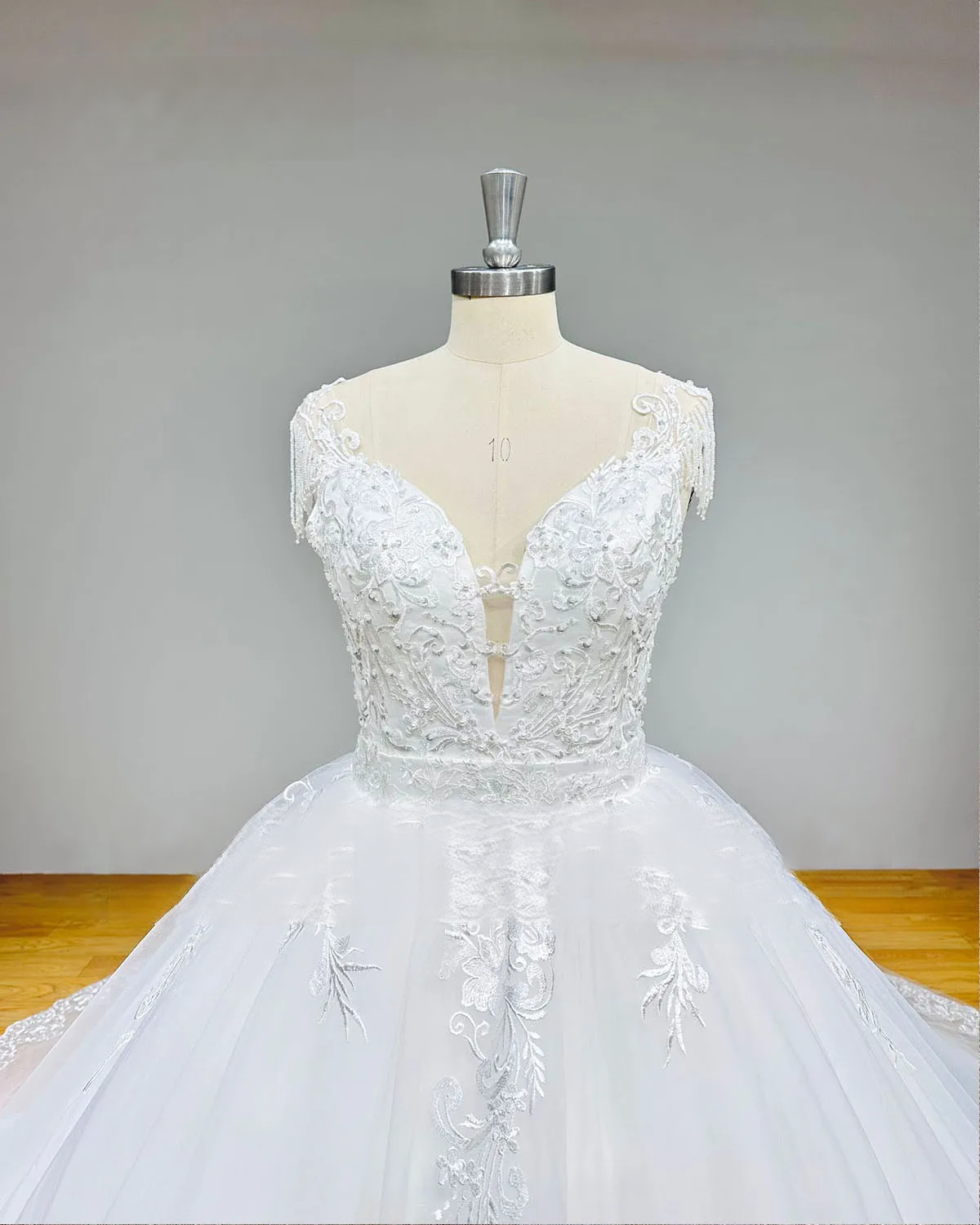 Close-up of a V-neck wedding dress bodice on a mannequin with heavy lace appliqués, shimmering sequins, and handcrafted beadwork.
