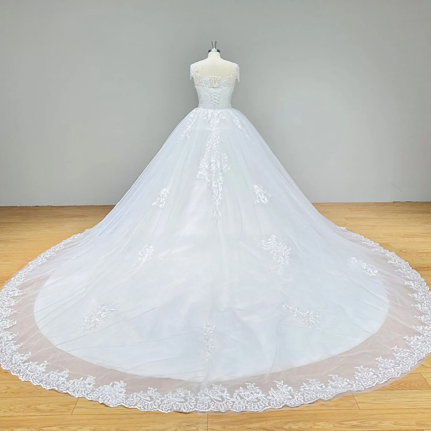 Back view of a wedding dress on a mannequin highlighting the expansive reach of a wide, lace-bordered detachable chapel overskirt.