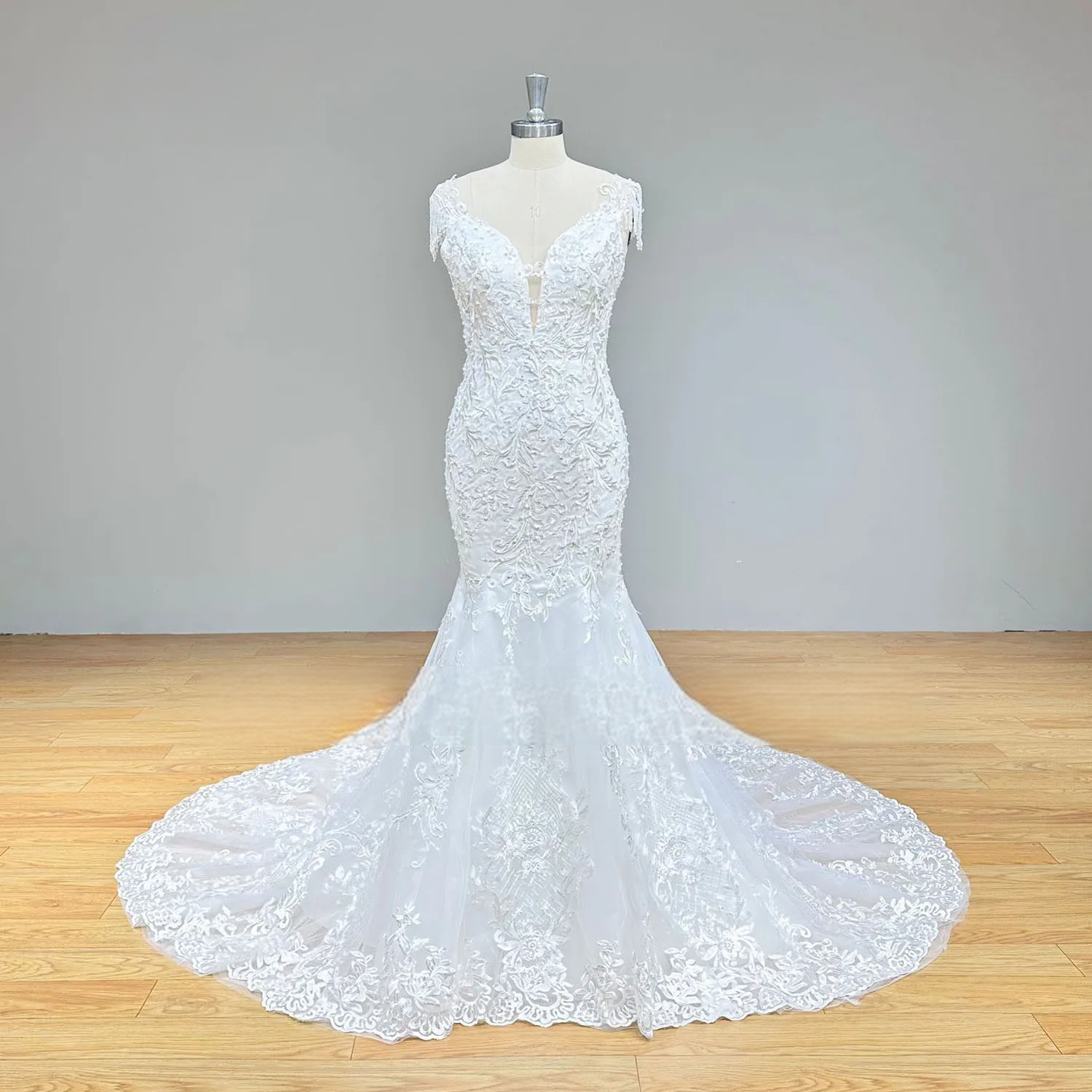 Full-length front view of a white mermaid wedding dress on a mannequin with all-over lace appliqués, beading, and a classic flared hem.
