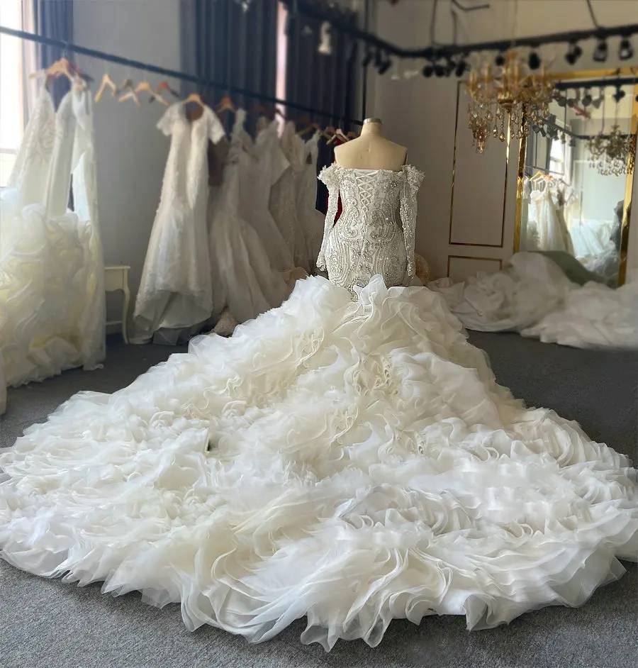 Side-angle shot of a plus-size beaded mermaid wedding dress, focusing on the structured long sleeves and the dramatic silhouette created by the detachable overskirt.