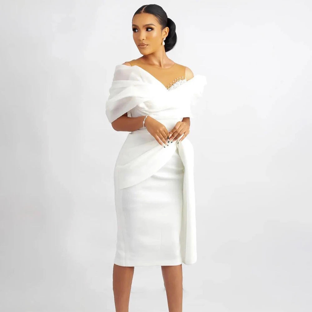 Modern off-the-shoulder white short wedding dress featuring an asymmetric draped organza overlay, a structured knee-length sheath silhouette, and delicate crystal beaded accents on an illusion neckline.