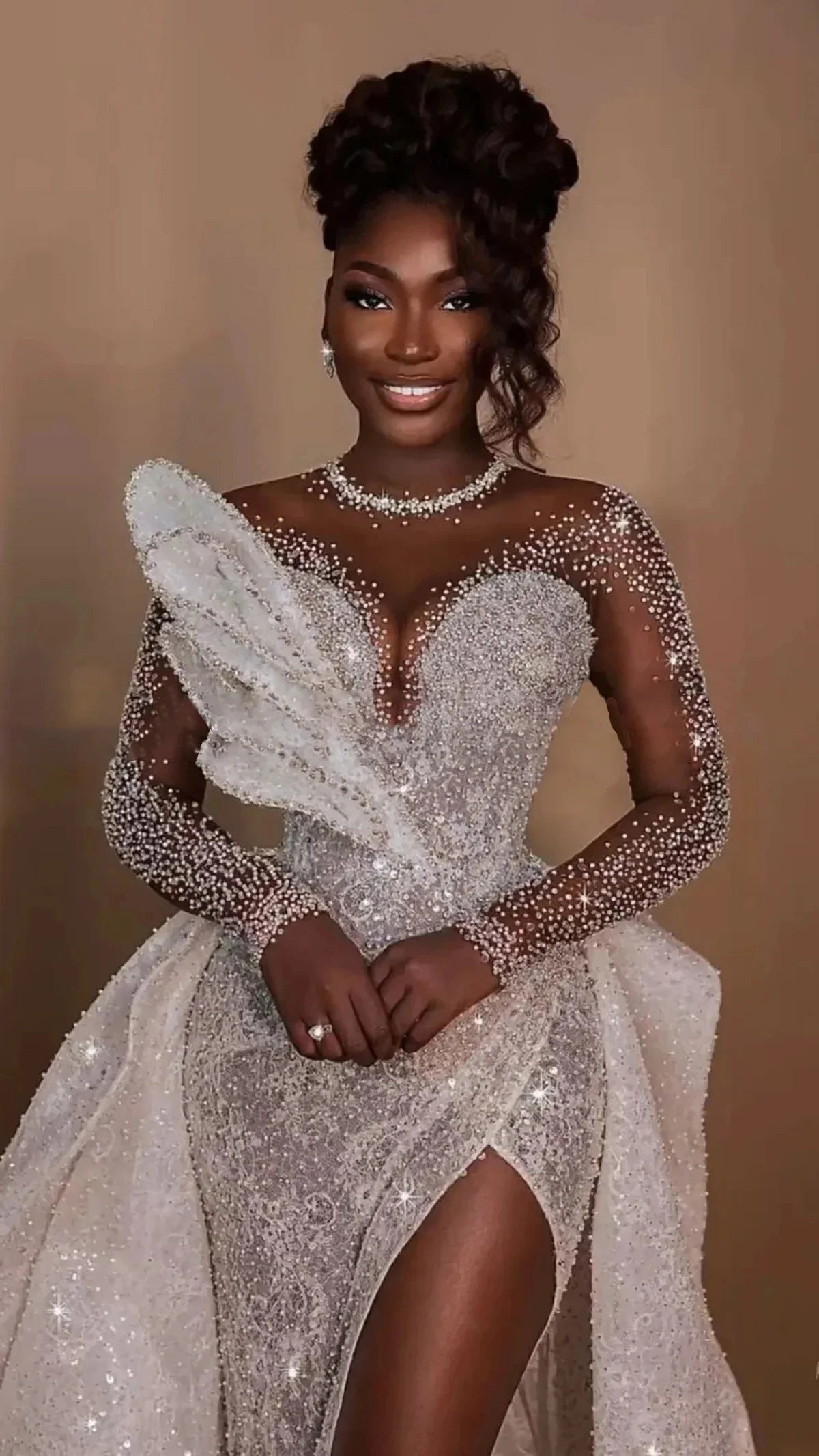 Plus size sparkly mermaid wedding dress with sheer net long sleeves, featuring a plunging sweetheart neckline, heavy rhinestone dust embellishments, and a sculptural 3D shoulder ruffle.