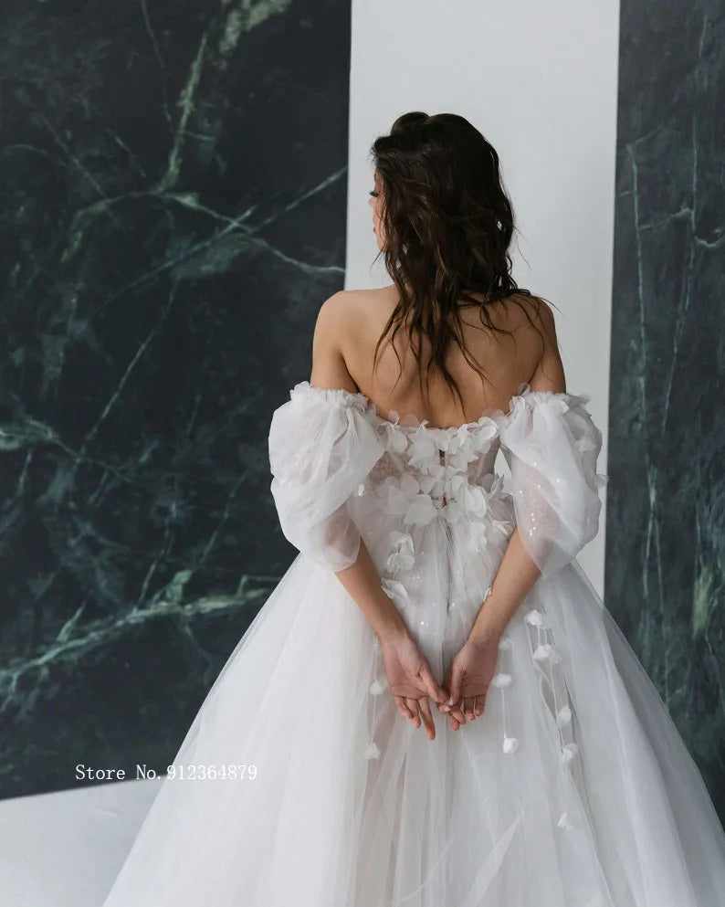 Beautiful bridal gown with an open back, intricate applique details, and detachable off-shoulder sleeves in a clean, modern studio setting.