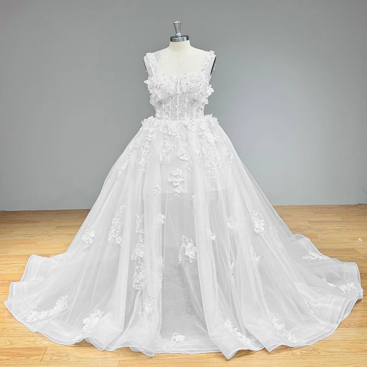 Classic princess-style ball gown bridal dress with a sheer embellished corset top and a floating layered tulle skirt on a mannequin. Description: An alternate front view of the gown under neutral studio lighting.