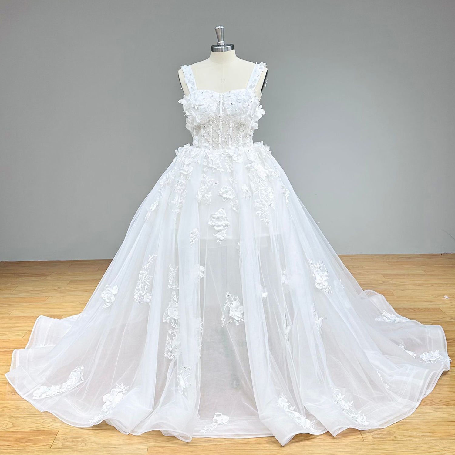 Front view of a princess tulle ball gown bridal dress with a structured exposed boning bodice and cascading 3D lace flowers on a dress form.