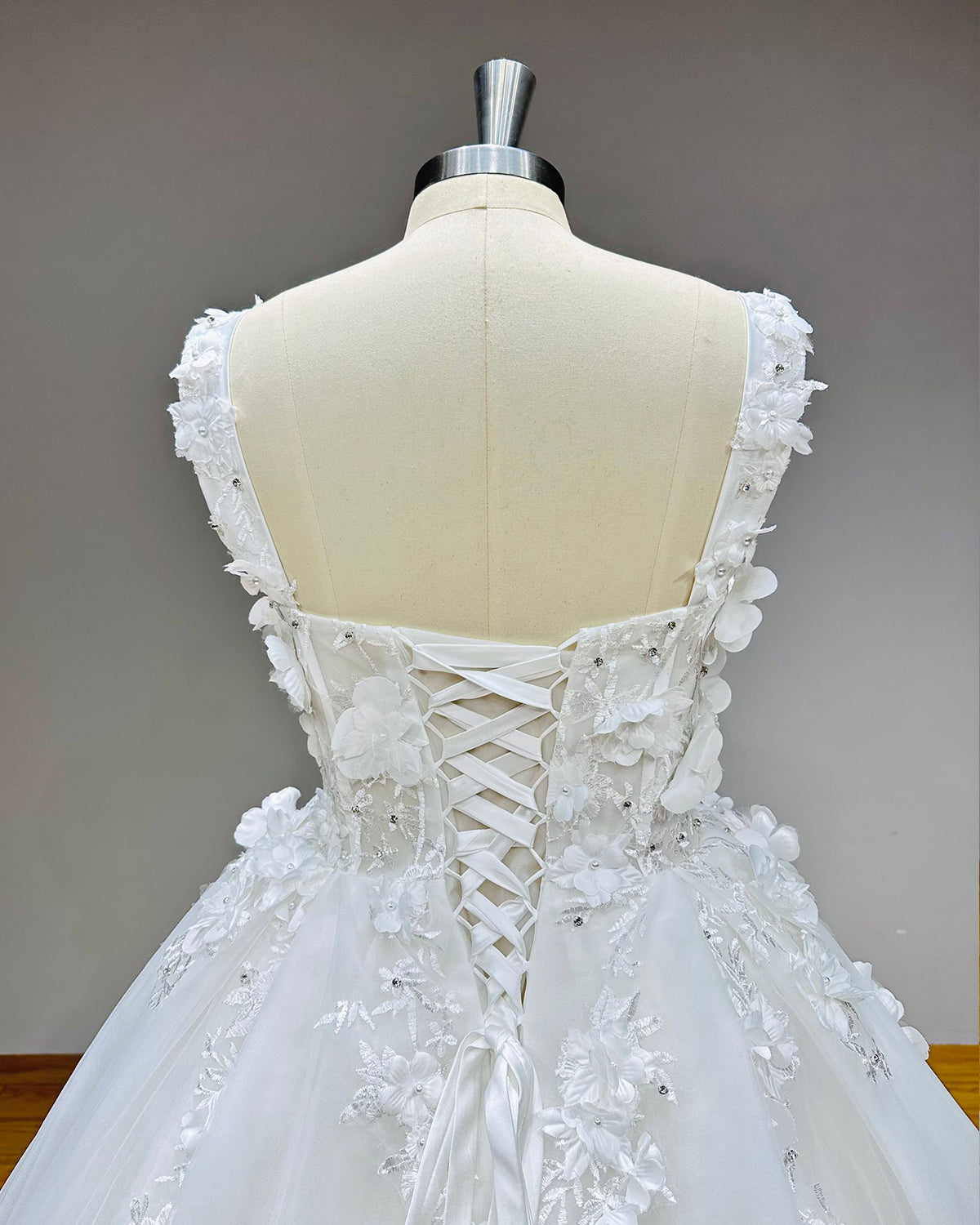 Close-up of the back of a bridal dress showcasing an adjustable satin lace-up corset back framed by 3D floral appliques and crystals.