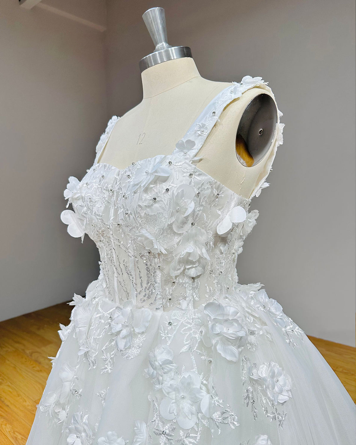 Side angle close-up of a wedding dress bodice emphasizing the sheer mesh corset panels, silver sequined beadwork, and layered fabric flowers.