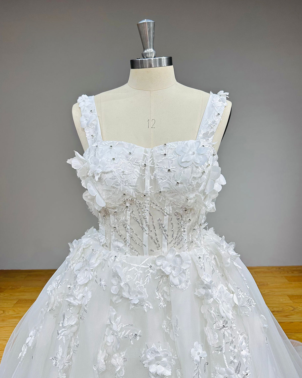 Detailed front view of a square-neck bridal bodice featuring dense 3D floral embroidery, delicate pearl beading, and sparkly rhinestone accents.