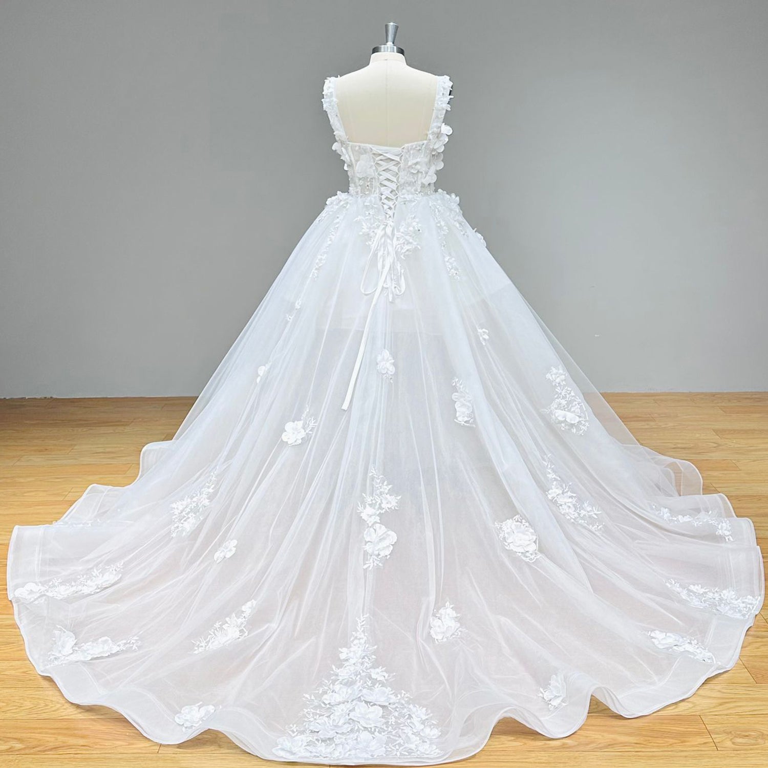 Full back view of a tulle ball gown wedding dress highlighting a traditional corset back closure and a sweeping train adorned with floral borders.