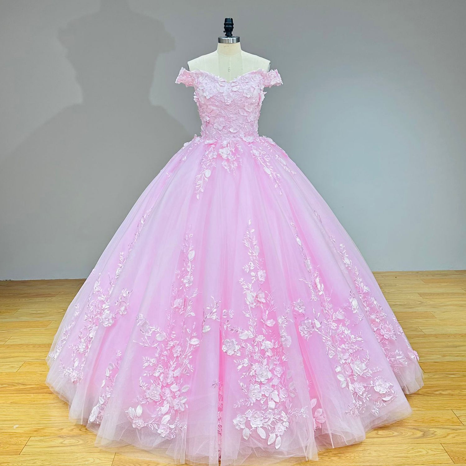 Detailed studio shot of a pastel pink princess bridal dress bodice with textured fabric flowers and embroidered leaves over a structured corset.