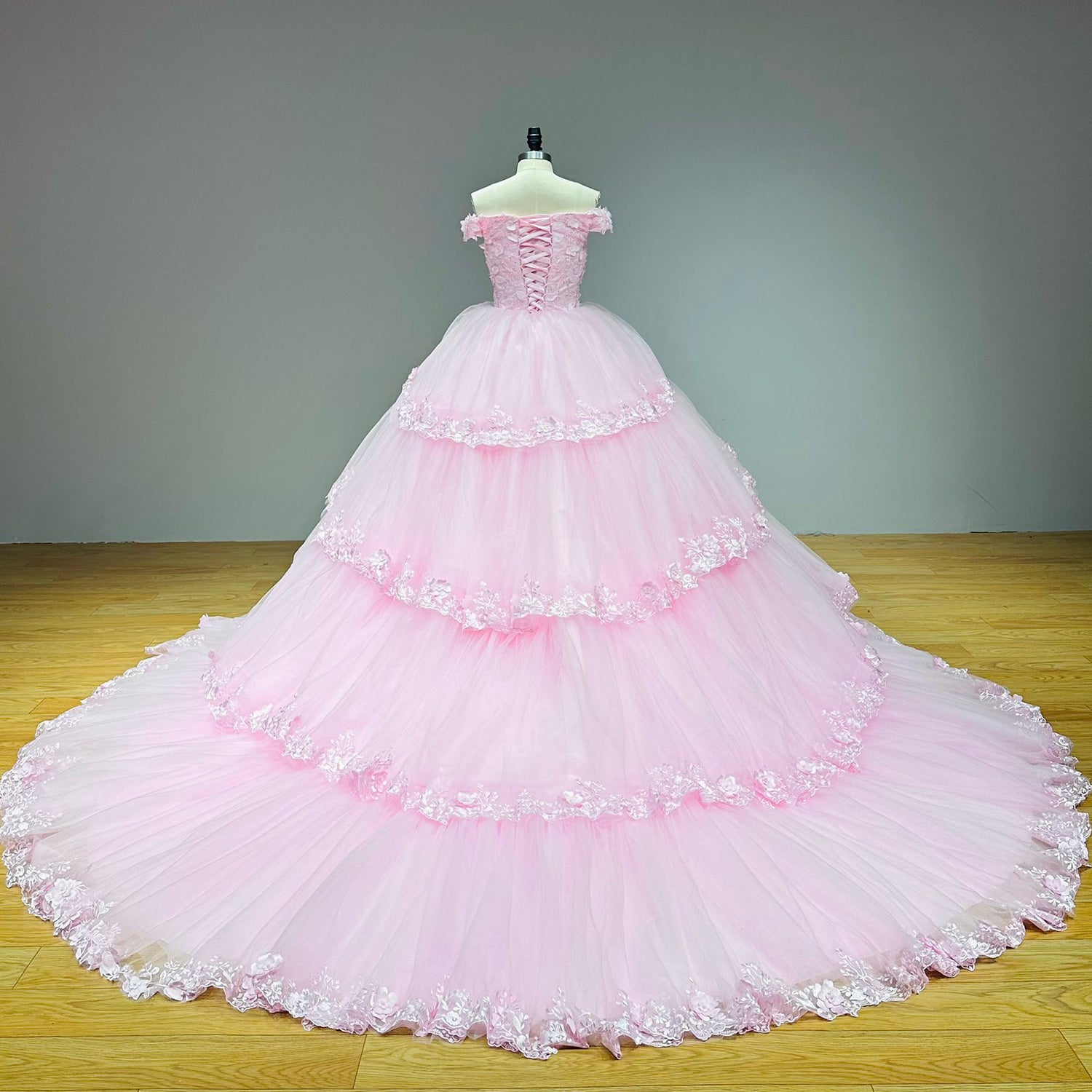 Full back view of a pink tulle princess wedding gown on a dress form, showcasing the classic corset ribbon closure and cascading floral train details.