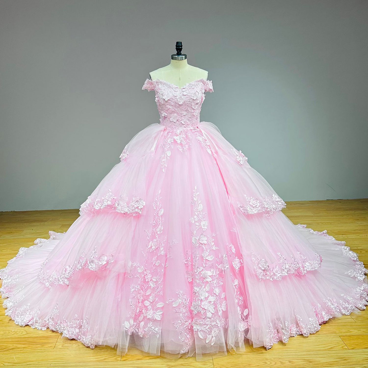 Full-length front view of a luxury pink princess ball gown wedding dress with a layered ruffle skirt on a mannequin.