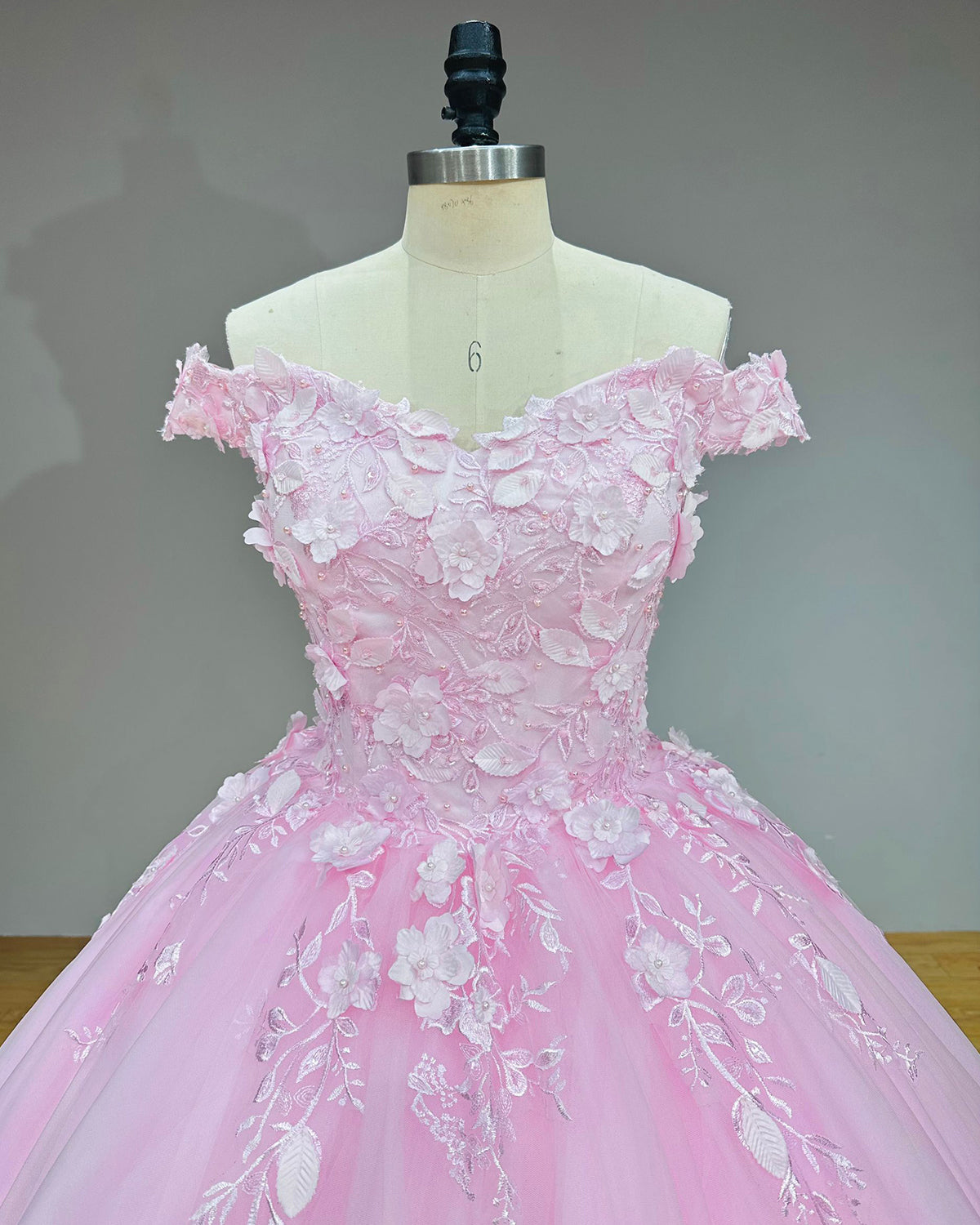 Rear view detail of a pink ball gown on a dress form, highlighting the adjustable lace-up corset back and the attachable scalloped lace edge train.