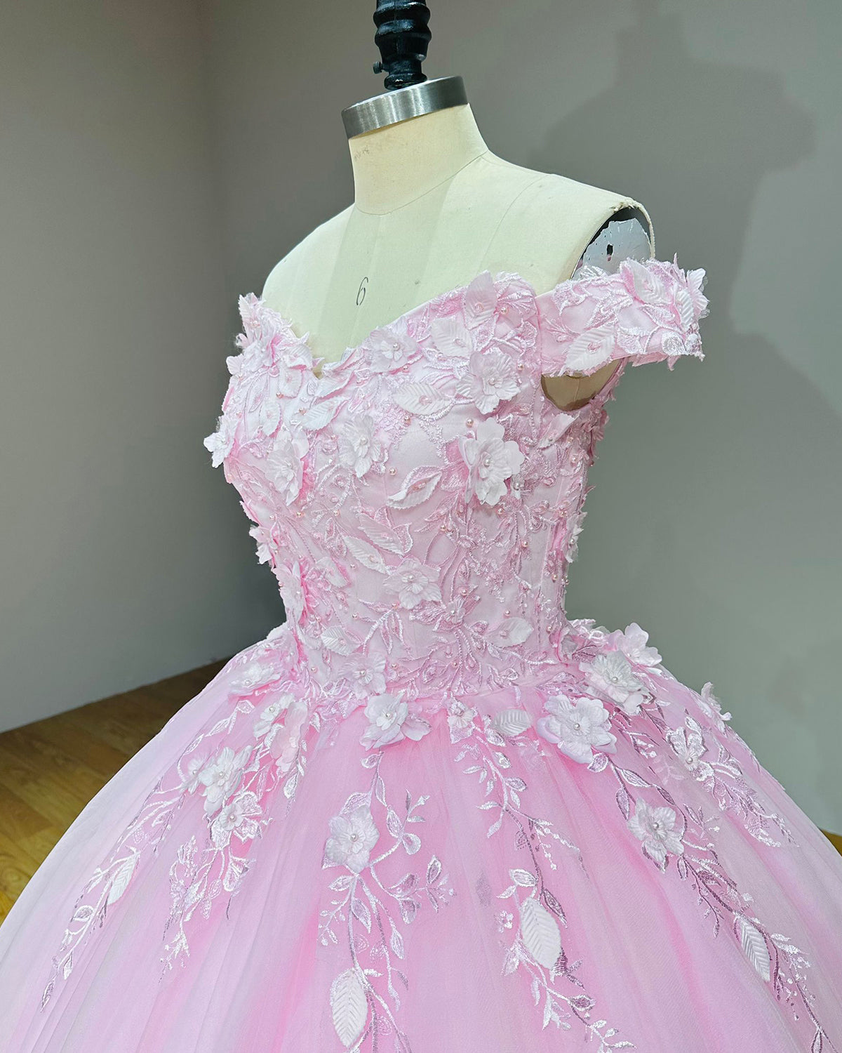 Side angle view of a pink off-the-shoulder wedding dress bodice on a mannequin, emphasizing the delicate 3D floral lace clusters and sequin accents.