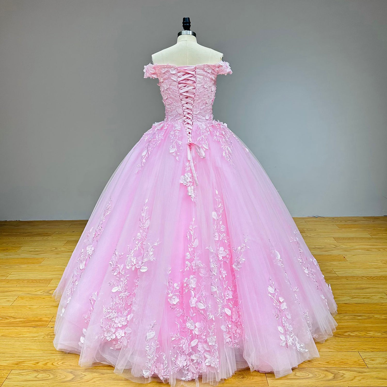 Full back view of a pink tulle princess wedding gown on a dress form, showcasing the classic corset ribbon closure and cascading floral train details.